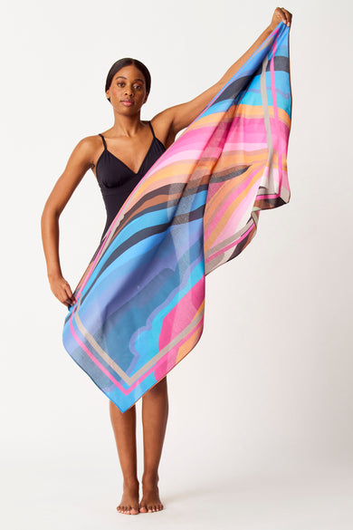 Multikleurige strandkleding van SUNSET STUDIO, met een opvallend geometrisch patroon, gedragen door een vrouw in een zwart badpak.
