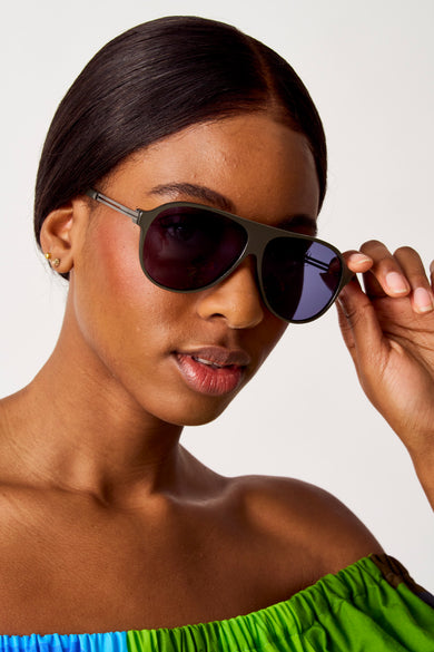 Lunettes de soleil vertes de SUNSET STUDIO, portées par une femme avec un haut off-shoulder en vert et bleu.