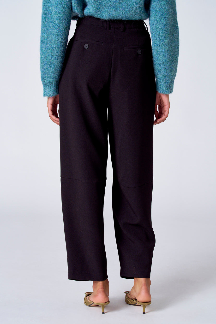 Pantalon de costume noir de SUNSET STUDIO, vu de par derrière, avec des détails de boutons et associé à un pull bleu.