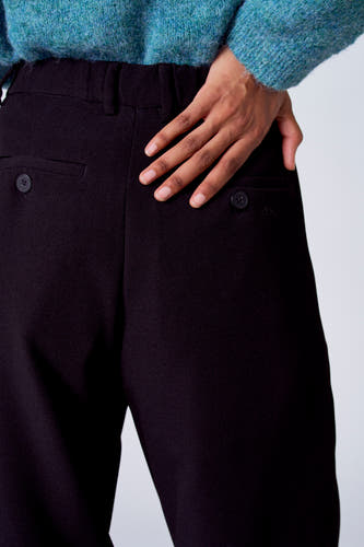 Zwarte kostuumbroek van SUNSET STUDIO, met zakken op de achterkant en een hand op de broek.
