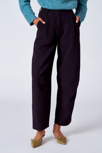 Pantalon de costume noir de SUNSET STUDIO, avec des poches à l'arrière et une main sur le pantalon.