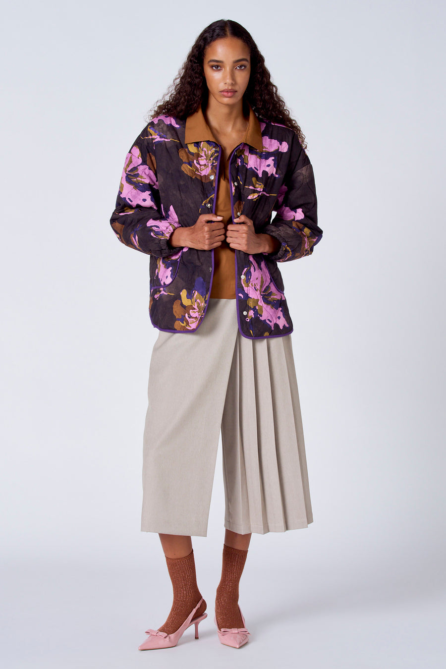 Bruine blouse met lange mouwen van SUNSET STUDIO, gedragen onder een bloemenjasje met beige culottes, bruine sokken en roze schoenen.
