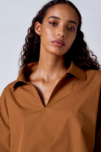 Bruine blouse met lange mouwen van SUNSET STUDIO, met een open kraag en lange gekrulde donkere haren.
