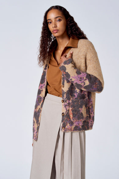 Bruine trui met V-hals van SUNSET STUDIO, gedragen onder een gebreid vest met bloemenprint en een beige rok.
