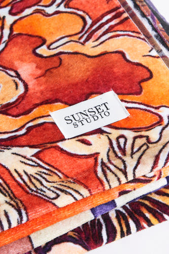 Oranje strandkleding van SUNSET STUDIO met een abstract bloemenpatroon en zichtbaar een merklabel.