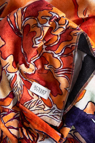 Oranje strandkleding van SUNSET STUDIO, met een abstract bloemmotief in rode en oranje tinten en een zwarte rand.