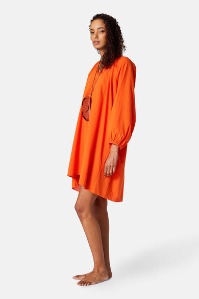 Oranje kleedje met lange mouwen van SUNSET STUDIO, met een bruin lederen tasje aan een koord.