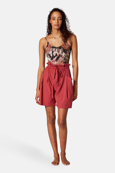 Veelkleurig badpak van SUNSET STUDIO, met een bladmotief en gedragen met rode shorts met strikceintuur.
