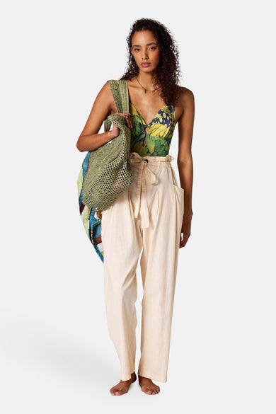 Pantalon beige de SUNSET STUDIO, avec taille paperbag et détail de cordon, associé à un sac en tissu vert.