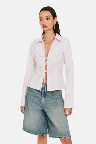 Roze overhemd met lange mouwen van TALLY WEIJL, met striksluiting, gecombineerd met een denim short en gouden sieraden.
