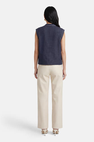 Blauw mouwloos gilet van ADORE, met witte stiksels, gecombineerd met crèmekleurige leren broek en hoge hakken.
