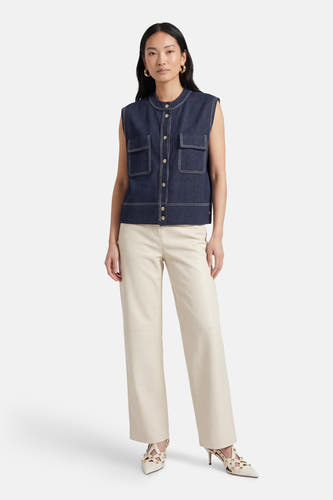 Mouwloze korte gilet van ADORE, met contrasterende stiksels en gedragen met crèmekleurige broek en hakken.