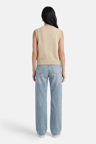 Beige trui van ADORE, met ronde hals en mouwloos design, gecombineerd met een lichtblauwe jeans en witte schoenen.