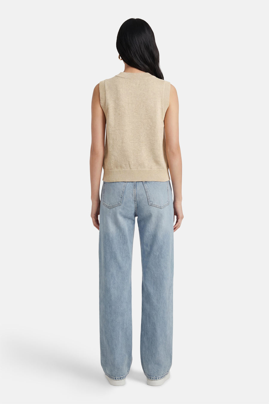 Beige trui van ADORE, met ronde hals en mouwloos design, gecombineerd met een lichtblauwe jeans en witte schoenen.