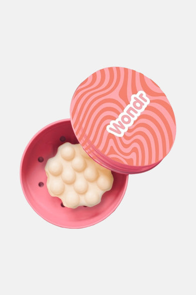 Multikleurig verzorgingsproduct van WONDR CARE, in een roze bakje met bolletjes en een gedessineerd deksel.
