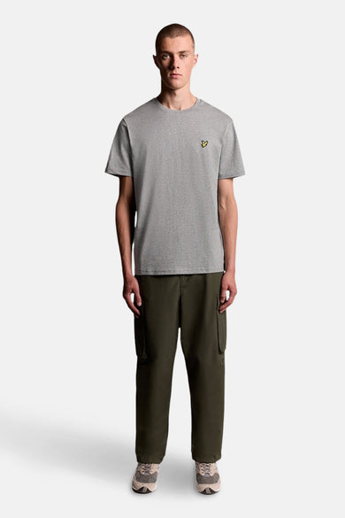 T-shirt gris à manches courtes de LYLE & SCOTT avec logo oiseau jaune, porté par un mannequin avec un pantalon cargo vert foncé.