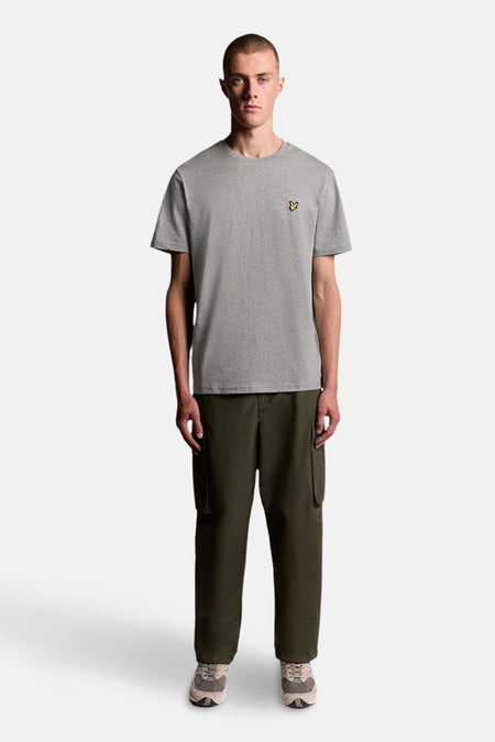 T-shirt gris à manches courtes de LYLE & SCOTT avec logo oiseau jaune, porté par un mannequin avec un pantalon cargo vert foncé.