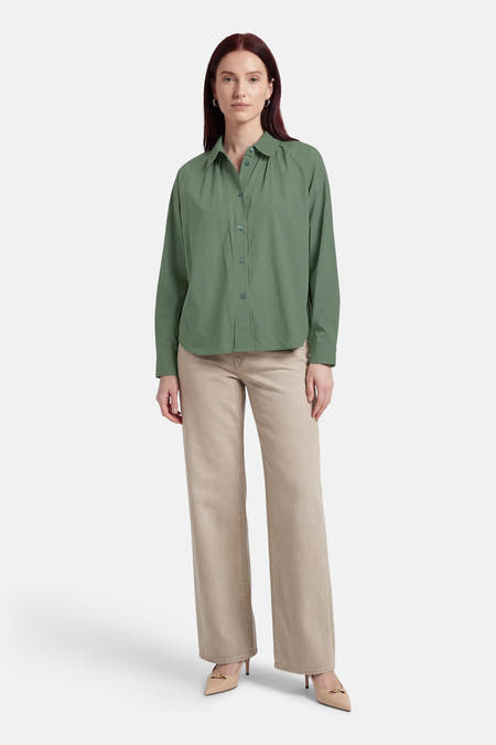 Chemise verte ADORE, à manches longues, portée avec un pantalon beige et des escarpins.