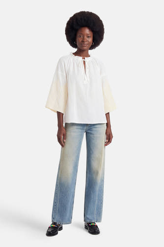 Witte blouse met lange mouwen van ADORE, met geborduurde mouwen en strikdetail aan de hals, gedragen met wijde jeans en zwarte loafers, front view.