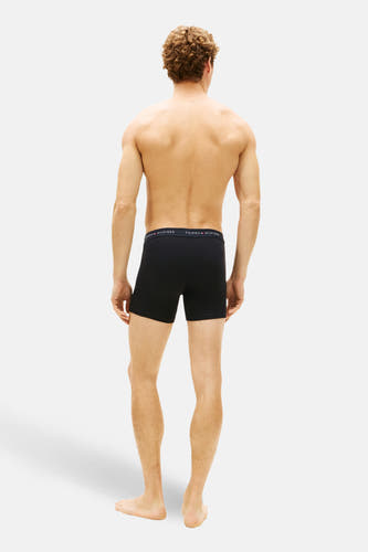 Boîtes noires de TOMMY JEANS, vues de l'arrière, portées par un homme aux cheveux bouclés.