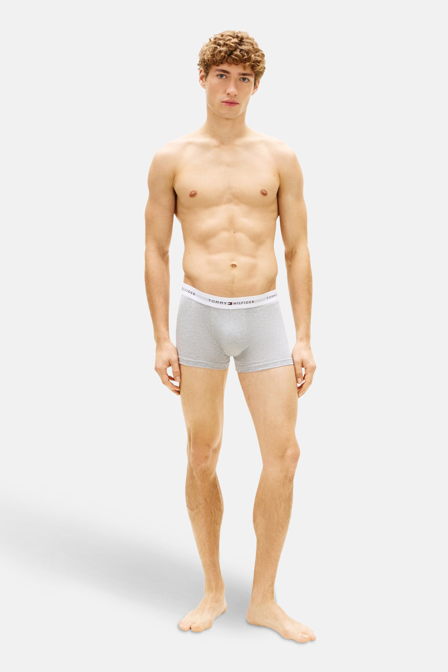 Grijze boxershort van Tommy Hilfiger, gedragen door een man met een gespierd bovenlijf, op een witte achtergrond.
