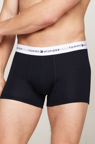 Blauwe boxershort van TOMMY JEANS met een witte tailleband met logo, in een close-up beeld.
