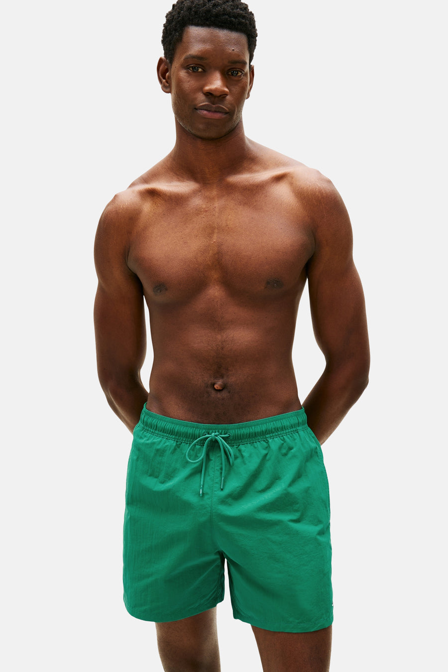Short de bain vert Tommy Hilfiger, porté par un homme les mains dans les poches.