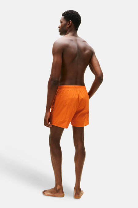 Oranje zwemshort van Tommy Hilfiger, gezien van achteren op een man met blote rug.