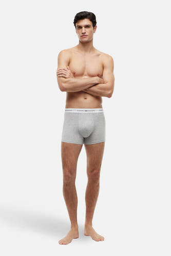 Grijze boxershort van TOMMY JEANS, gedragen door een man met gekruiste armen en blote voeten.
