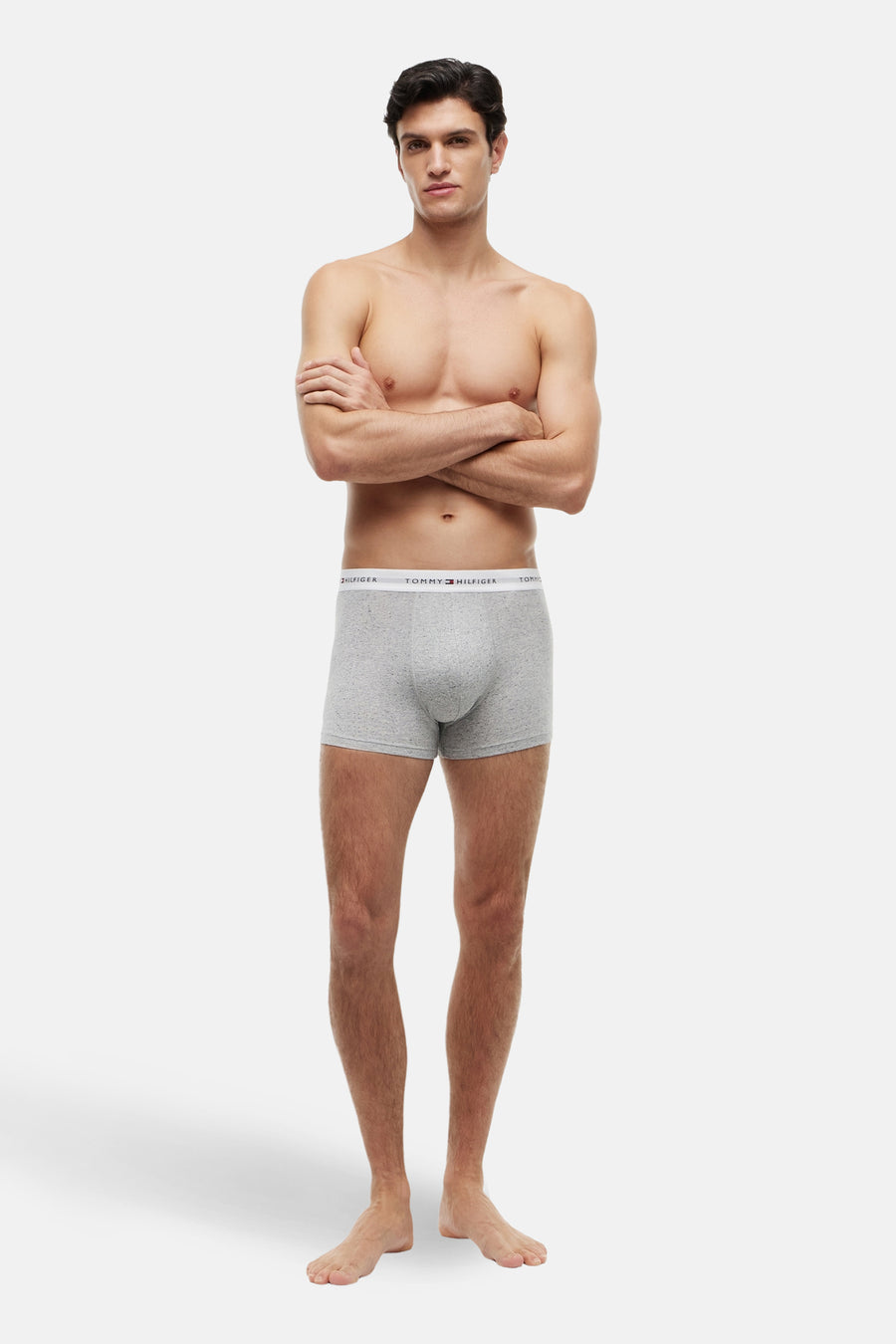 Grijze boxershort van TOMMY JEANS, gedragen door een man met gekruiste armen en blote voeten.
