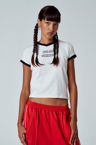 T-shirt blanc à manches courtes et col noir d'Unwind, avec le texte "Endless Weekends" et porté avec un short de sport rouge.