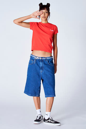 Rood T-shirt met korte mouwen van Unwind, gedragen met wijde jeansshorts en zwarte schoenen met witte sokken.