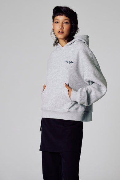 Grijze sweater met kap van Unwind, met zakken aan de voorkant en gedragen met een zwarte rok.
