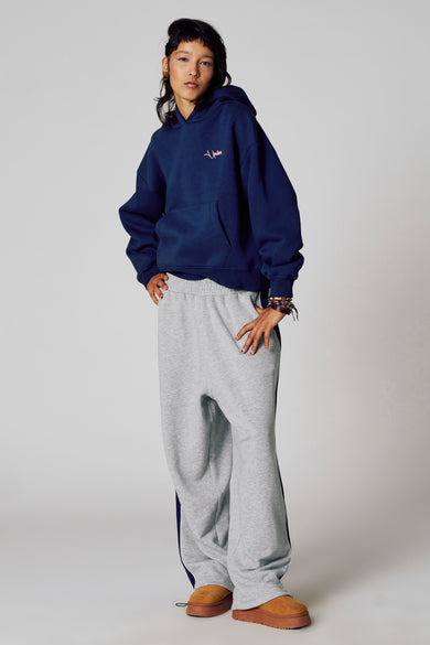 Pull-over bleu avec capuche d'Unwind, porté avec un short de jogging gris et une bande bleue foncée et des chaussures brunes.