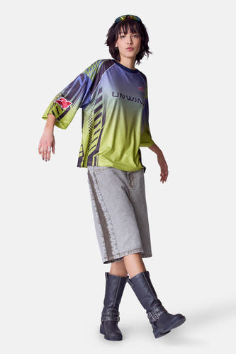 Groen T-shirt met korte mouwen van Unwind, met kleurverloop en grafische patronen, gedragen met denim shorts en zwarte laarzen.

