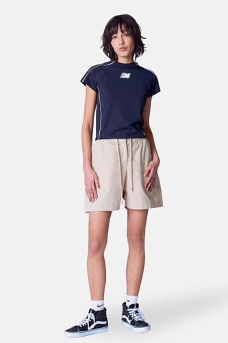 Beige short van Unwind, met trekkoord en gedragen met een donkerblauw shirt en zwarte sneakers.
