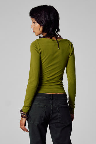 T-shirt vert avec manches longues d'Unwind, associé à un pantalon de corduroy foncé et des bracelets.