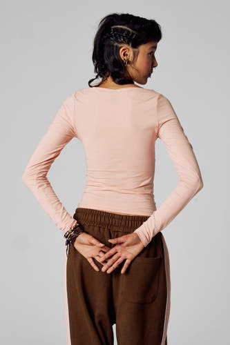 T-shirt rose à manches longues d'Unwind, avec des cheveux tressés et un short de jogging marron avec une bande rose.