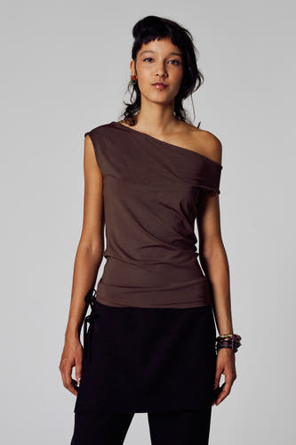 Bruin T-shirt met korte mouwen van Unwind, met asymmetrische halslijn, gedragen met een zwarte rok en kleurrijke armbanden.
