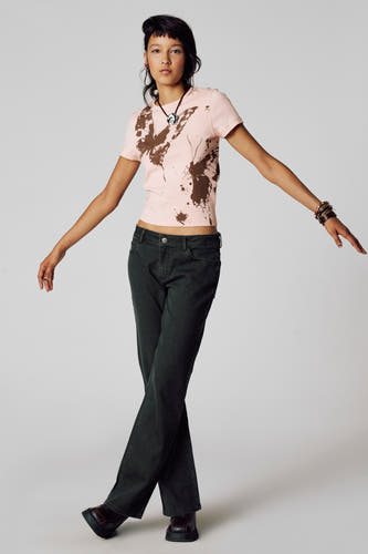 T-shirt rose à manches courtes d'Unwind, avec imprimé de papillon et porté avec un pantalon vert foncé et des bijoux.