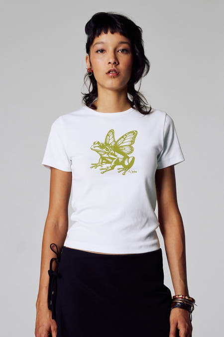 Wit T-shirt met korte mouwen van Unwind, met groene kikker en vlinder print, gedragen met een zwarte rok.
