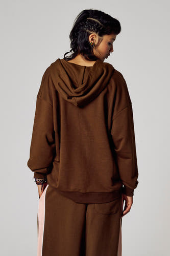 Bruin vest van Unwind, gezien van achteren, met capuchon en lange mouwen, gedragen met een bijpassende broek.