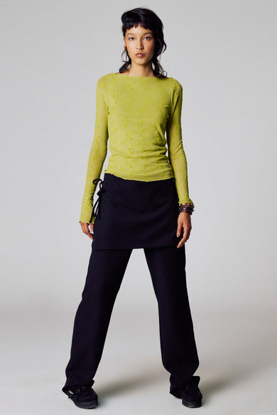 Groen T-shirt met lange mouwen van Unwind, met een subtiel patroon en gedragen met een zwarte broek en rok.
