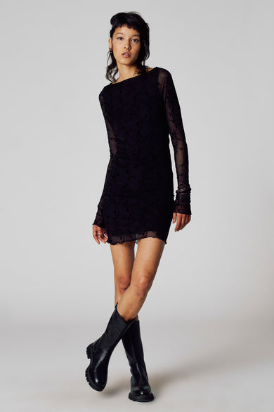 Robe noire à longues manches d'Unwind, avec un motif floral subtil et portée avec des bottes noires.