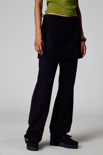 Pantalon noir d'Unwind, avec des jambes qui s'évasent et combiné avec un haut vert et des bracelets.