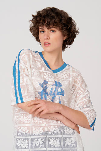 T-shirt blanc à manches courtes d'Unwind, avec des rayures bleues sur les épaules et un motif floral en dentelle.