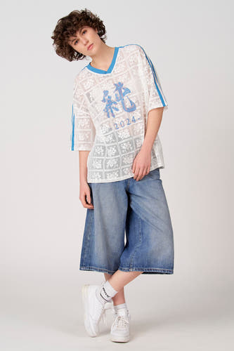 T-shirt blanc à manches courtes d'Unwind, avec détails bleus, motif en dentelle et imprimé bleu, combiné avec un jean ample et des baskets blanches.