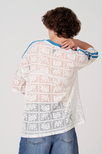 T-shirt blanc à manches courtes d'Unwind, avec motif floral en dentelle et accents bleus sur les manches et l'encolure.