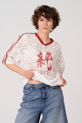 Wit T-shirt met korte mouwen van Unwind, met rode details en rode Chinese karakters erop, gecombineerd met een spijkerbroek.
