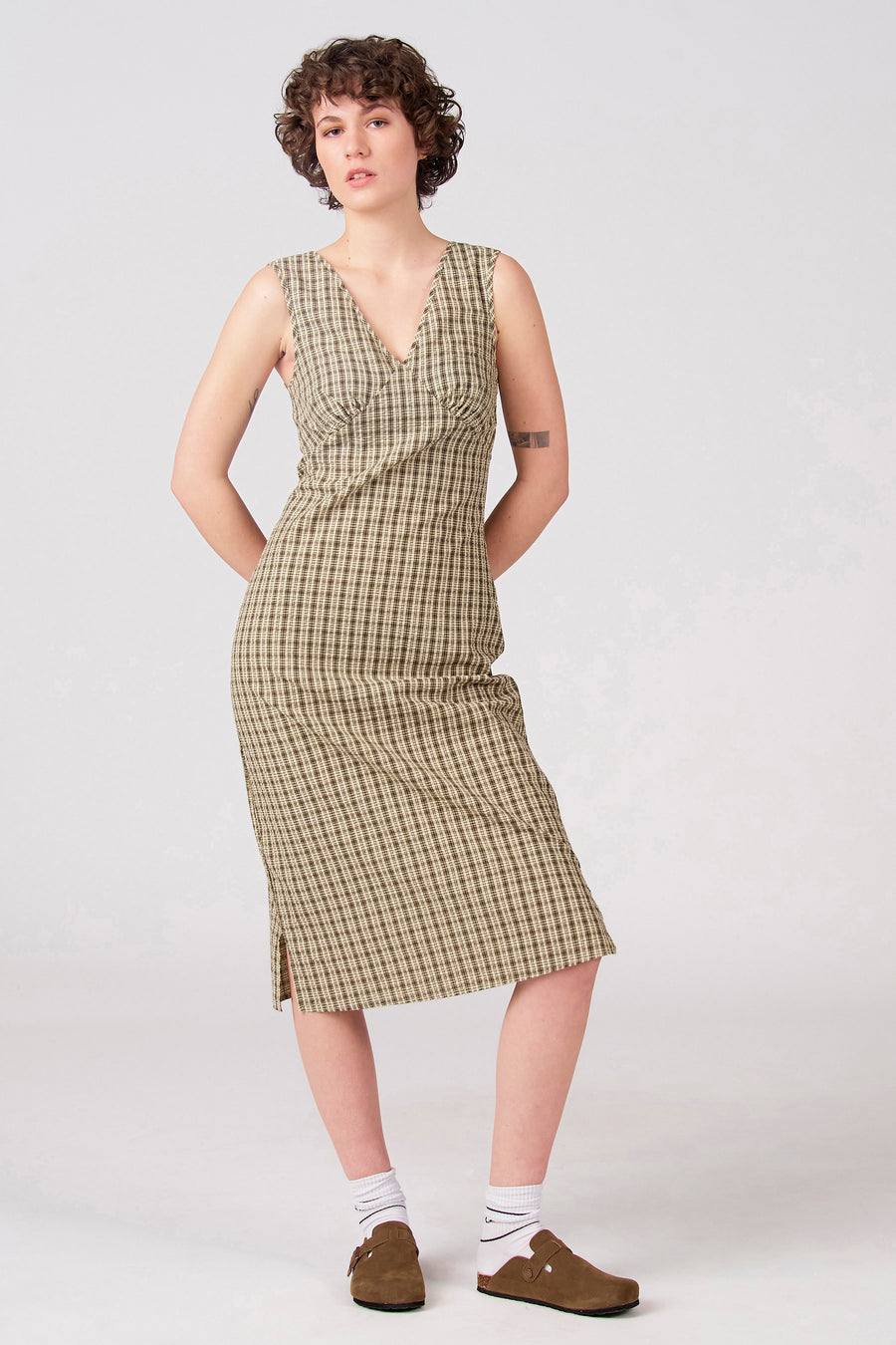 Robe verte sans manches d'Unwind, à motif à carreaux et avec une fente sur le côté, portée avec des chaussettes blanches et des chaussures marron.